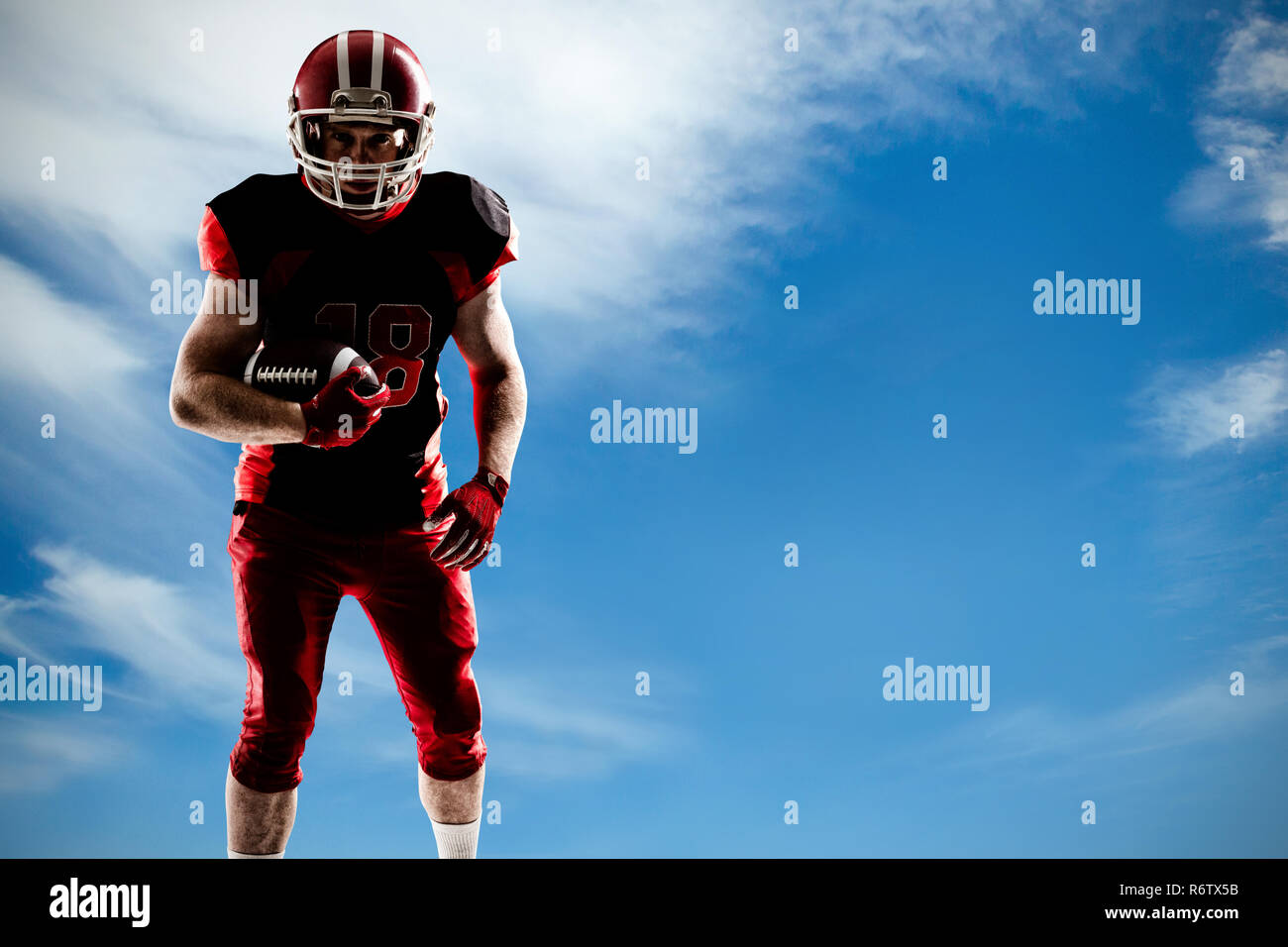 American football player stehend mit rugby ball und Helm gegen den Blick auf den blauen Himmel Stockfoto