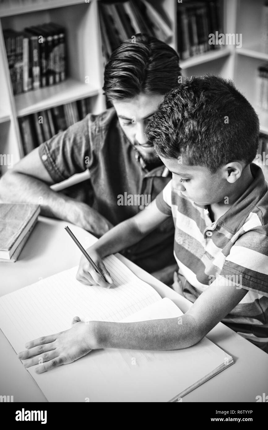 Lehrer helfen Schulkind mit seinen Hausaufgaben in Bibliothek Stockfoto