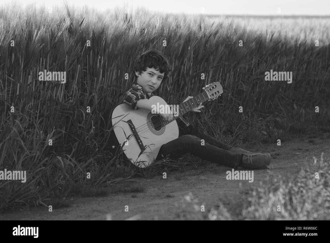 Ein Junge in Jeans und ein Hemd sitzt in das Feld mit einer Gitarre. Schwarz und Weiß. Matt Stilisierung. Stockfoto