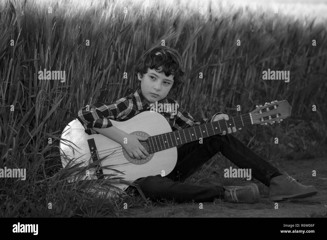 Ein Junge in Jeans und ein Hemd sitzt in das Feld mit einer Gitarre. Schwarz und Weiß. Stockfoto