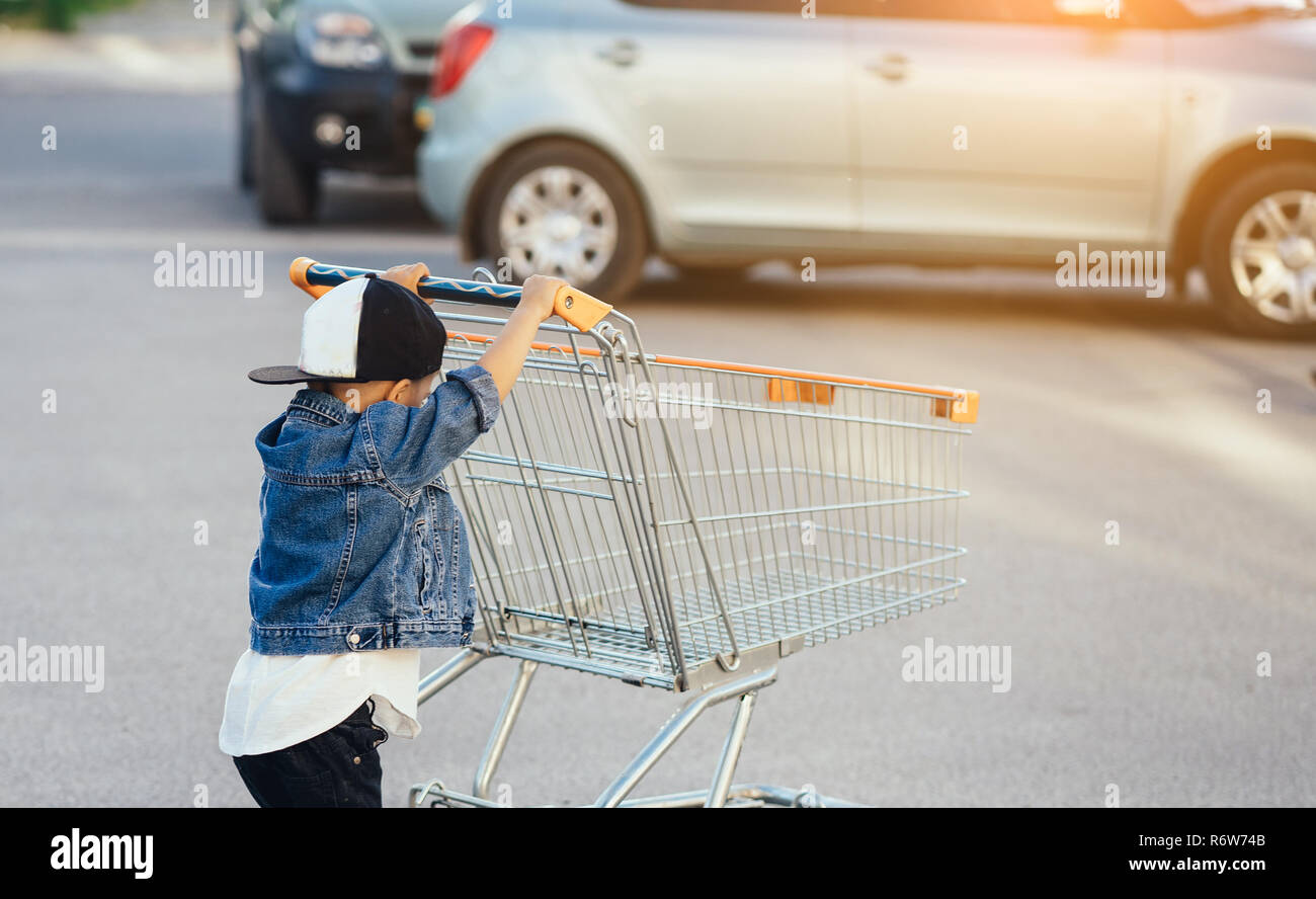 Ein kleiner Junge und ein großer Einkaufswagen auf dem Parkplatz Stockfoto
