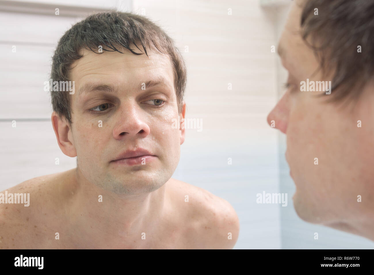 Ein glattrasierter junge Mann sieht im Spiegel Stockfoto