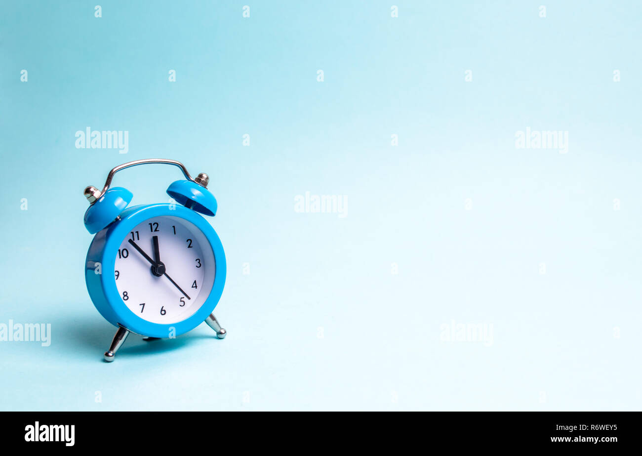 Ein blauer Alarm Clock auf einem hellblauen Hintergrund. Das Konzept der Wartezeit für ein Meeting, ein Datum. Pünktlichkeit. Die Kosten für die stündliche Arbeit eines Spezialisten, Bus Stockfoto