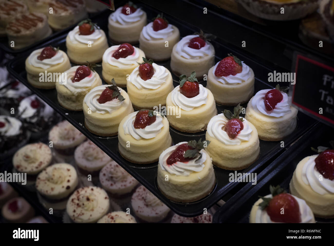 Fach der köstlichen, dekadenten Frischkäse Törtchen garniert mit Erdbeeren und Schlagsahne, in einer Vitrine in einem städtischen Markt. Stockfoto