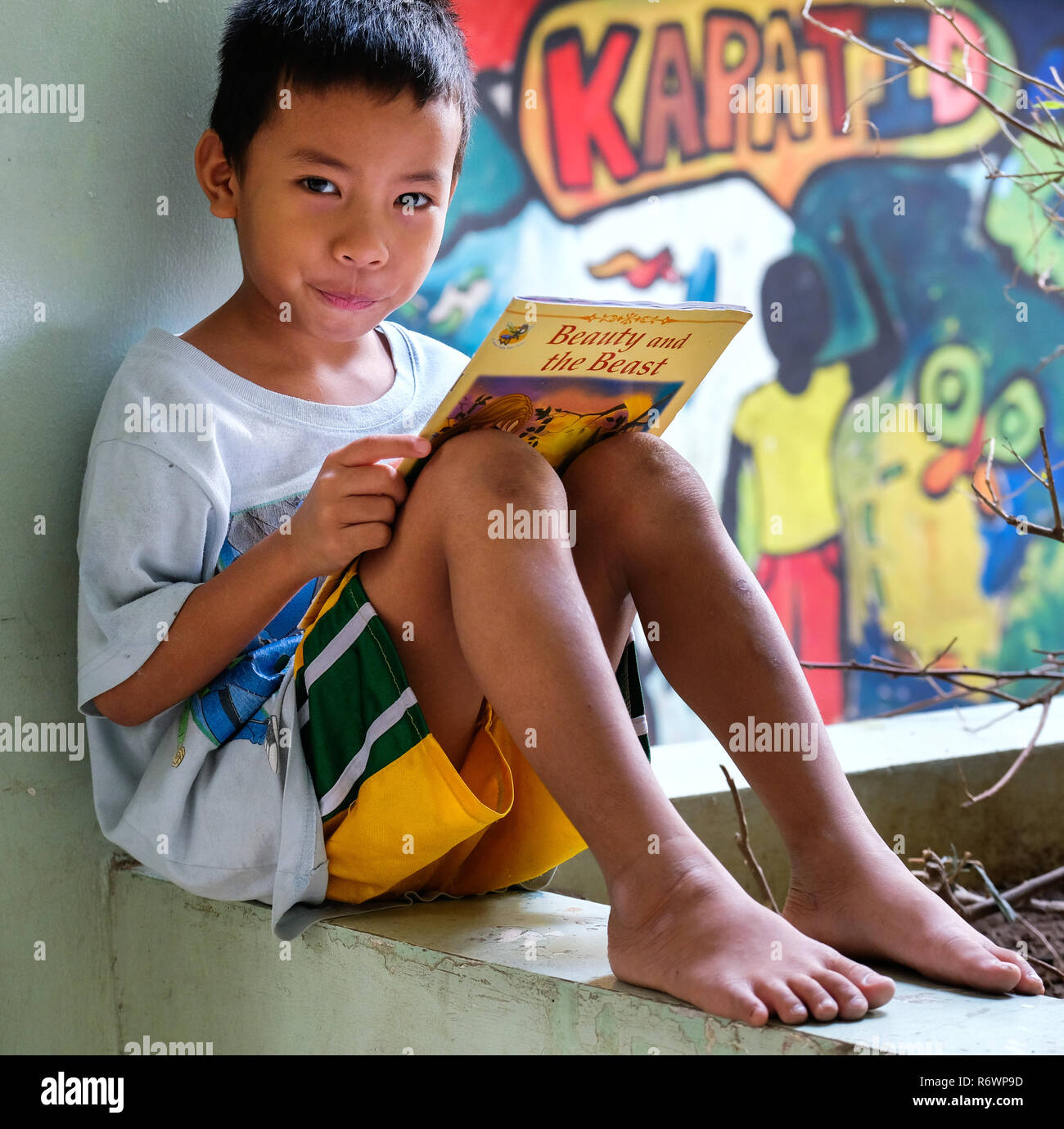 Straßenkind lese "Die Schöne und das Biest" in einem Bilderbuch vor einer Graffiti-wand im Kuya Zentrum für Straßenkinder in Quezon City, Metro Manila, Philippinen. Stockfoto