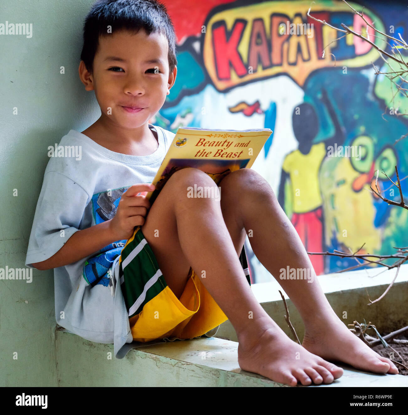 Straßenkind lese "Die Schöne und das Biest" in einem Bilderbuch vor einer Graffiti-wand im Kuya Zentrum für Straßenkinder in Quezon City, Metro Manila, Philippinen. Stockfoto