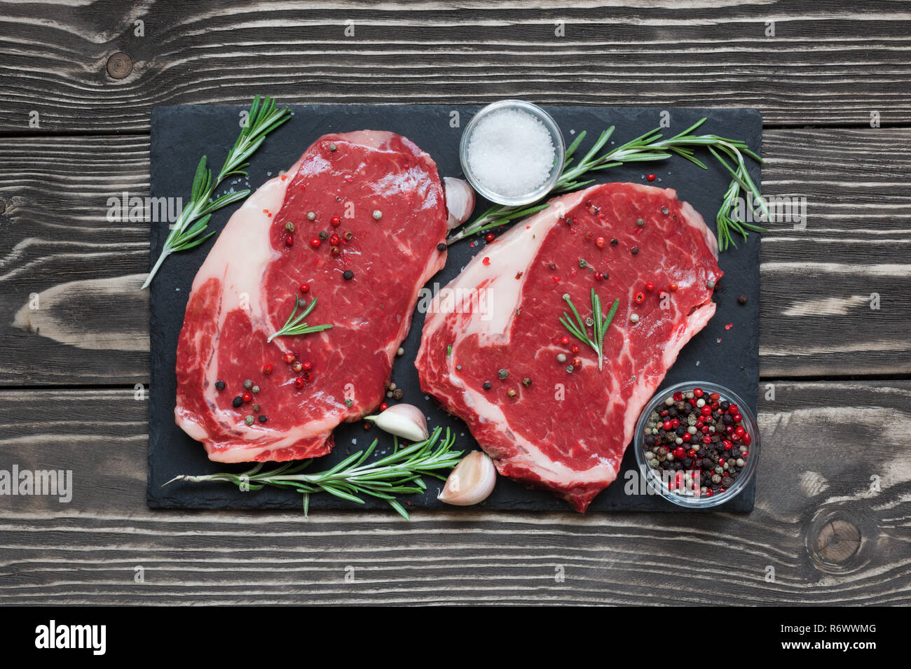 Rohes Rindfleisch Steak mit Gewürzen und Rosmarin auf schwarzem Schiefer Brett über Holz- Hintergrund. top View Stockfoto