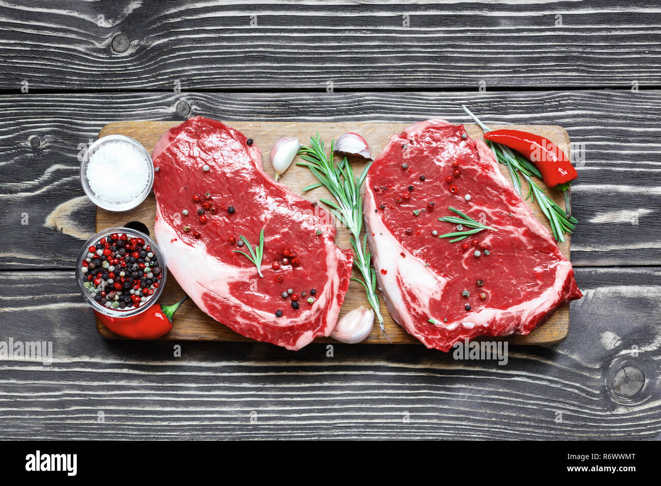 Rohes Rindfleisch Steak mit Gewürzen und Rosmarin auf Holz Schneidebrett über Holz- Hintergrund. top View Stockfoto