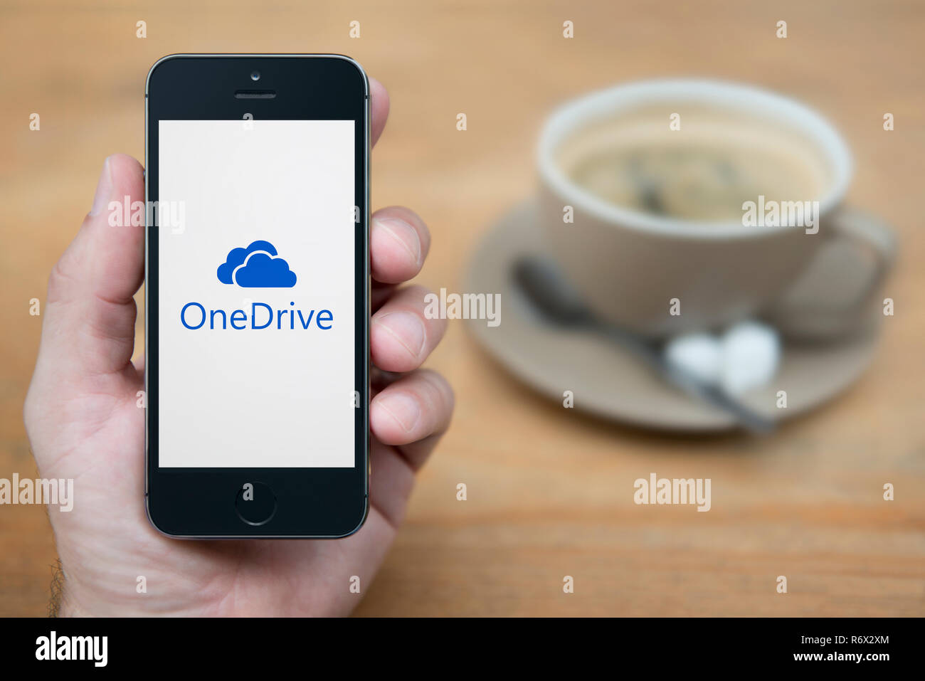 Ein Mann schaut auf seinem iPhone die zeigt den Microsoft OneDrive Logo (nur redaktionelle Nutzung). Stockfoto