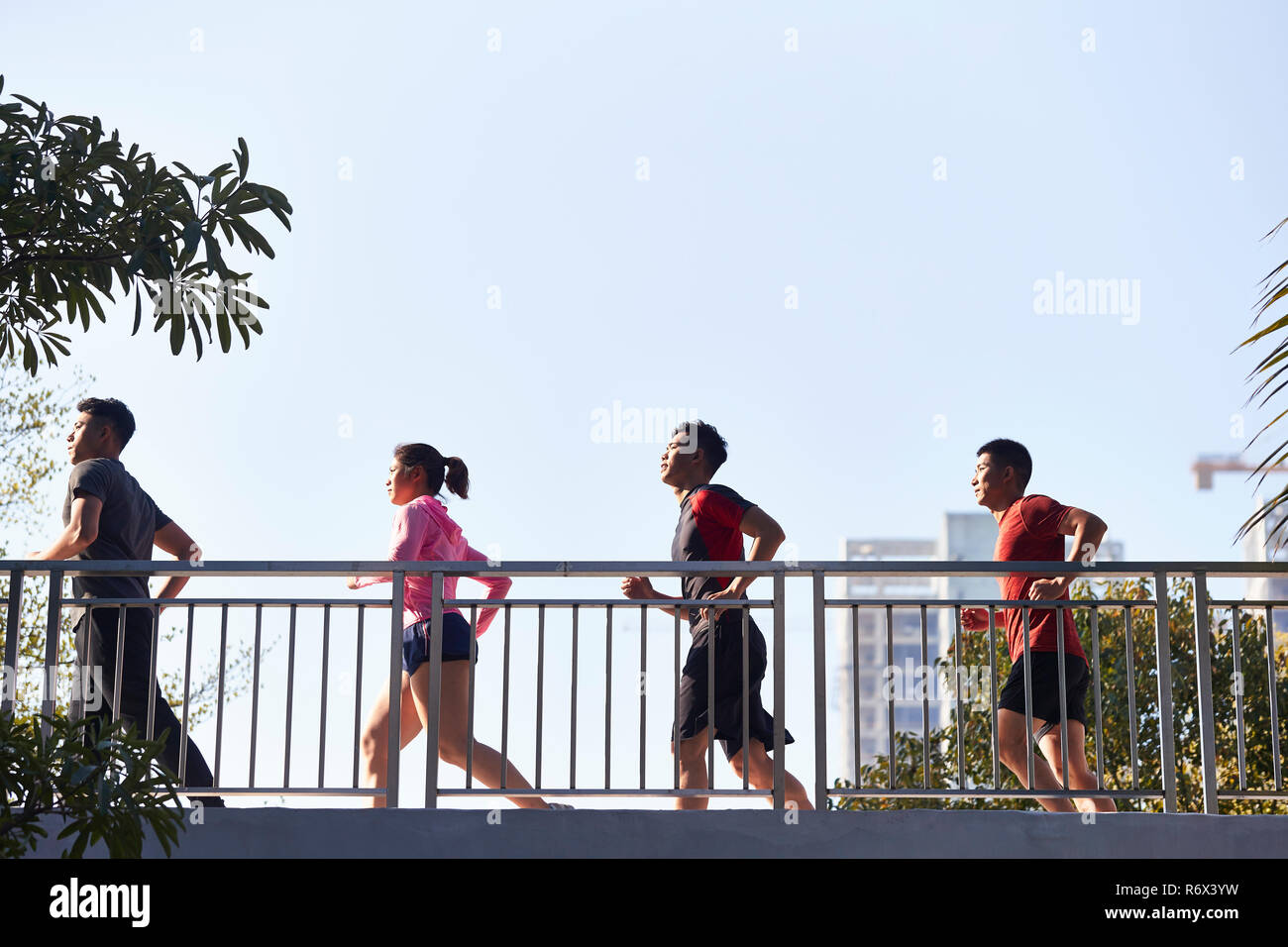 Vier junge asiatische Läufer am Morgen läuft durch eine Fußgängerbrücke. Stockfoto