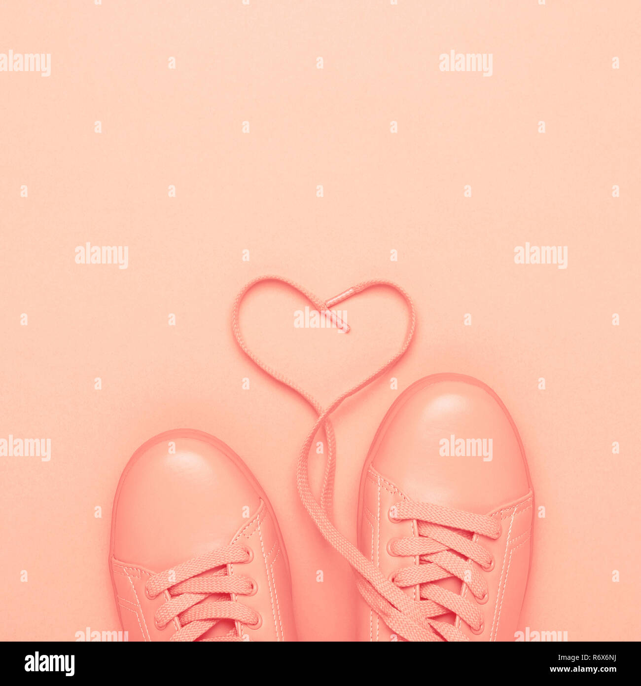 Paar coral Schuhe mit Herz aus Schnürsenkel auf Korallen Hintergrund. Trendy Pastelltönen, Schwarzweiß-Bild. Lebende Koralle Farbe des Jahres 2019. Stockfoto