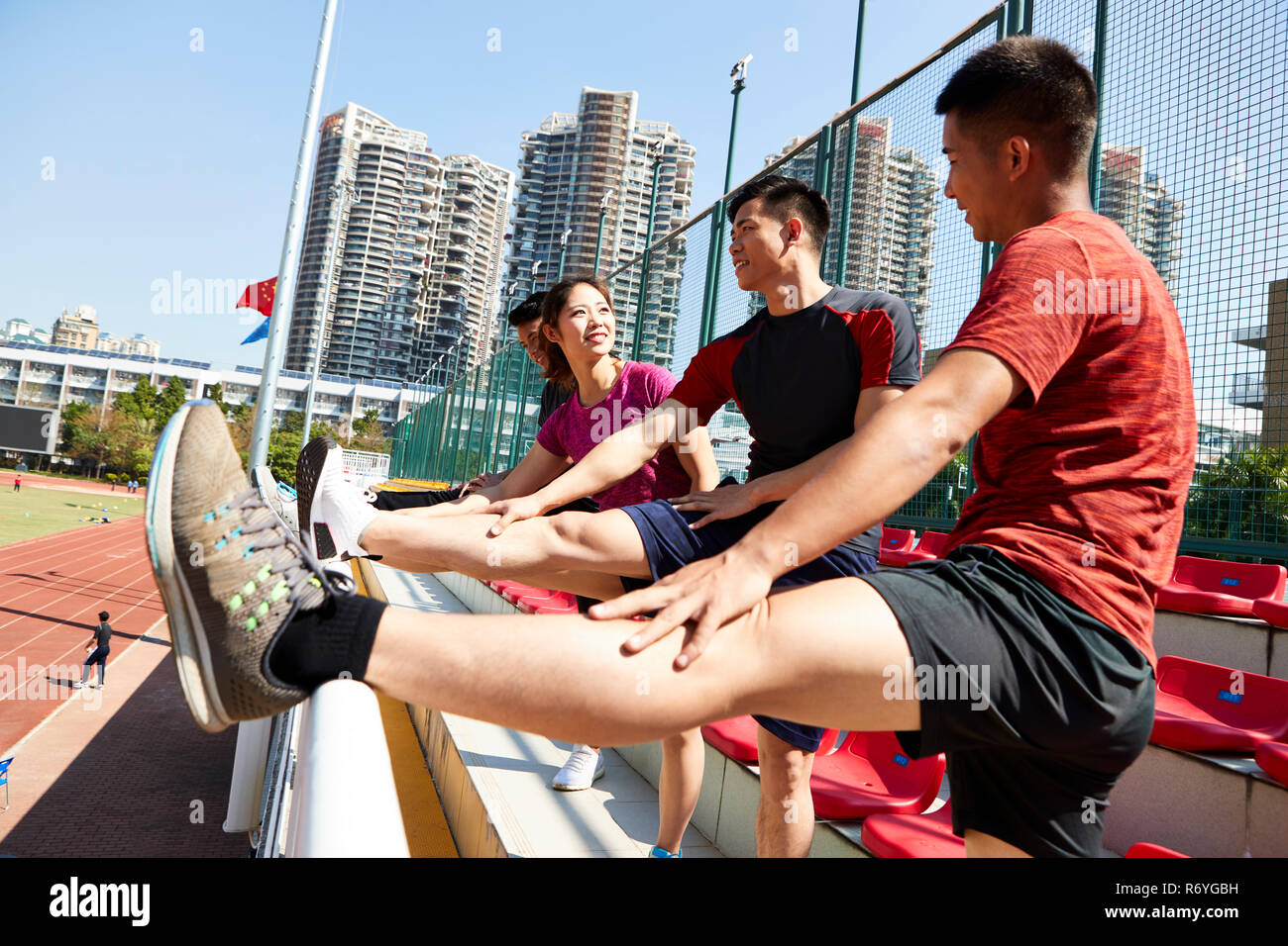 Gruppe von jungen asiatischen Sportler Aufwärmen drücken Beine im Stadion. Stockfoto