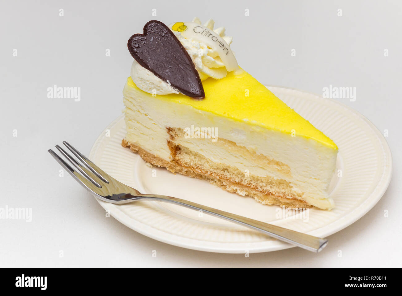 Zitronen- Käsekuchen mit Schokolade Herz serviert auf einem weissen Teller, beschriftet mit dem niederländischen Wort für Zitronen Stockfoto