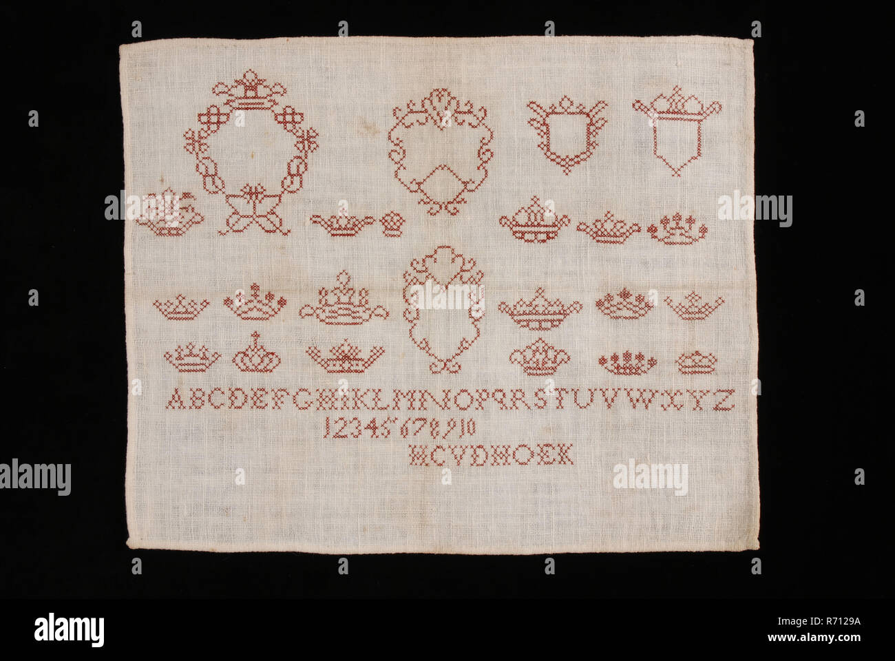 H.C. van der Hoek, Sampler arbeitete in Kreuzstich in dunklem Rot Seide auf Creme Baumwolle mit Leinen Effekt, markierte HCVDHOEK, sampler Stickereien Handarbeit bilder Seide Baumwolle, Textil stickerei Kreuzstich rechteckiges Stück gebleicht Baumwolle mit einer eingerückten Leinen Effekt in den Thread. Das Tuch hat Saum Rand von 0,4 cm Breit. Es gibt Gestickter auf dem Schoß in Kreuzstich mit Seide in dunklem Rot und in einzelnen Thread. Zwei Drittel der Patch gestickter ist mit stilisierten Tafeln und Kronen und den unteren Teil des Stückes besteht aus einem Alphabet aus 25 Buchstaben, den Buchstaben J fehlt es-Serie Stockfoto