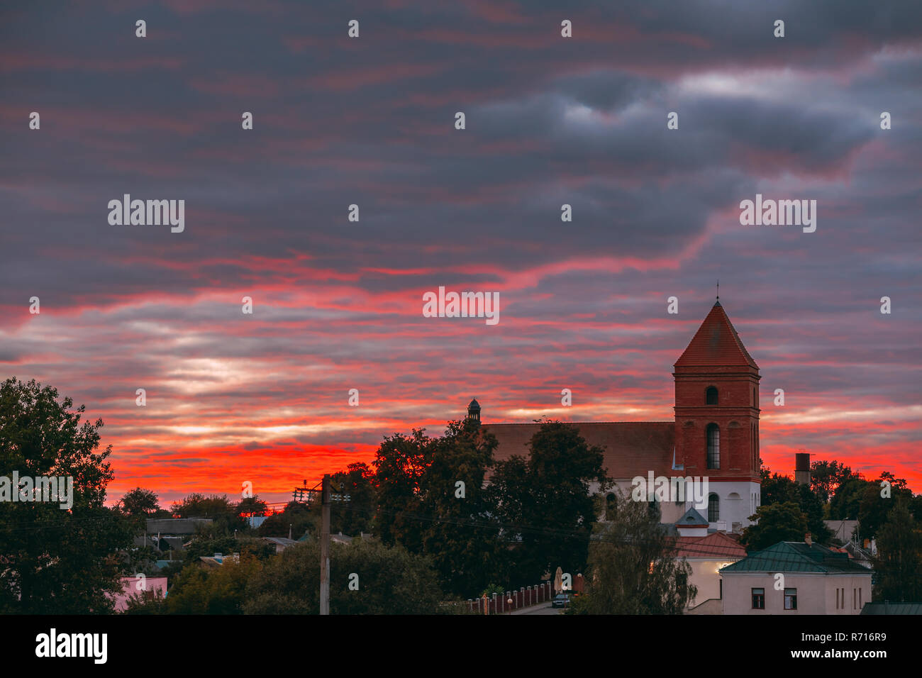 Mir, Belarus. Saint Nicolas Römisch-katholische Kirche in der Hintergrundbeleuchtung von erstaunlichen Sonnenuntergang über der Landschaft der Häuser des Dorfes. Das Wahrzeichen der Stadt. Historische Architektur Stockfoto