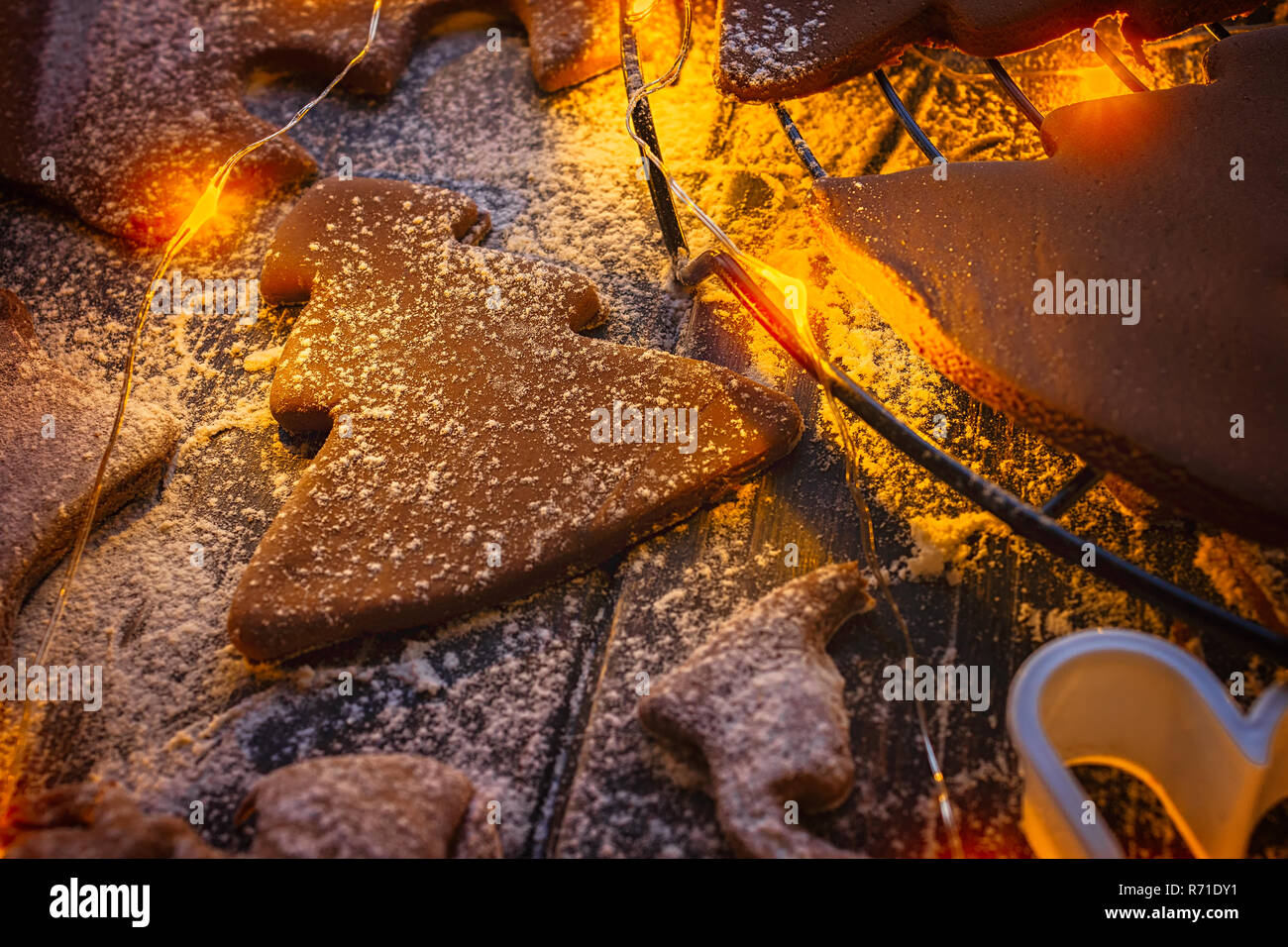 Weihnachtsplätzchen in verschiedenen Formen auf einem Küchentisch in warmes Licht aus Lichterketten Stockfoto