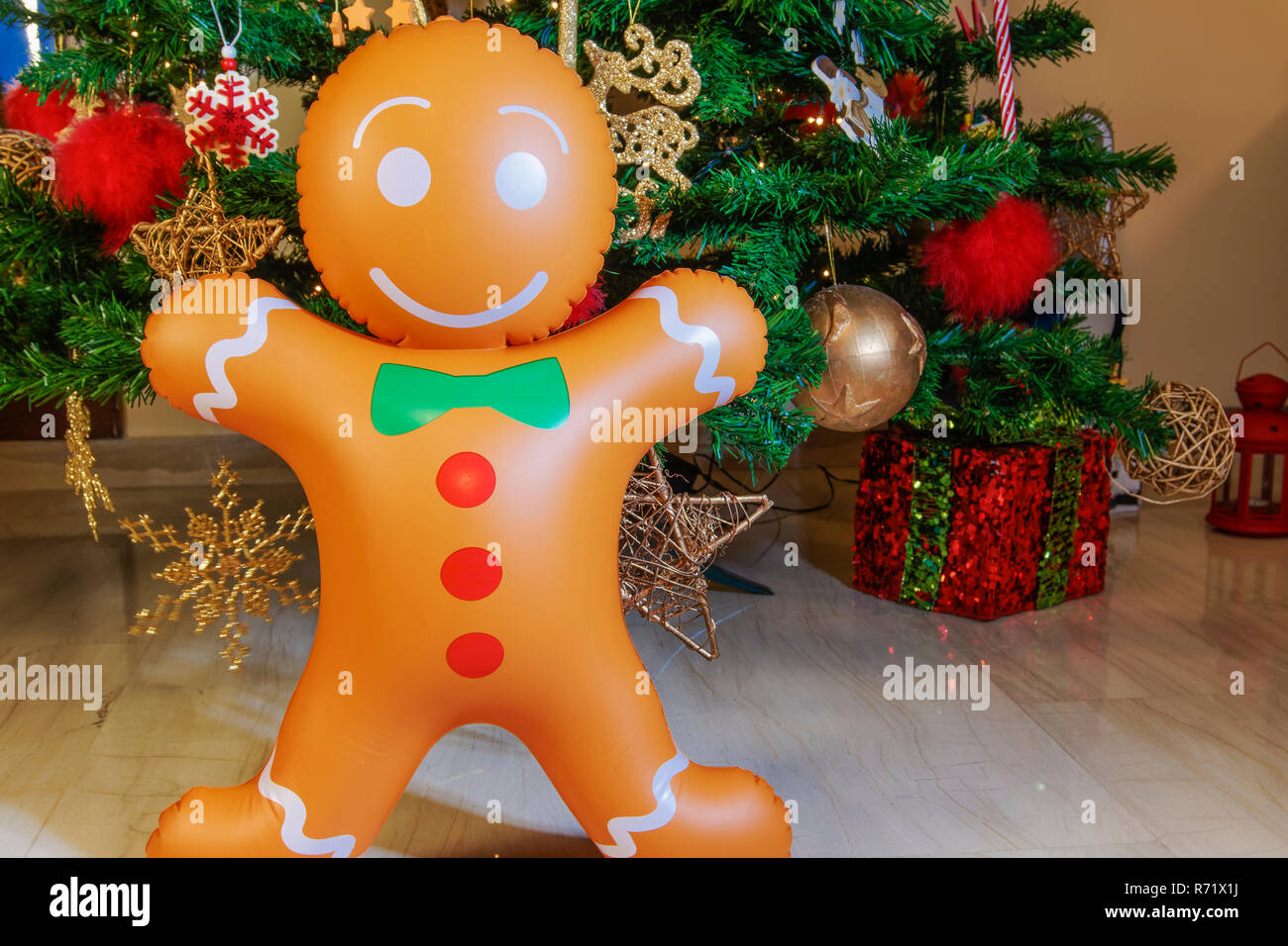 Große aufblasbare Gingerbread Man am Weihnachtsbaum. Luft ausgeblasen saisonale Abbildung vor dem beleuchteten künstlicher Weihnachtsbaum mit Beleuchtung & Dekorationen. Stockfoto