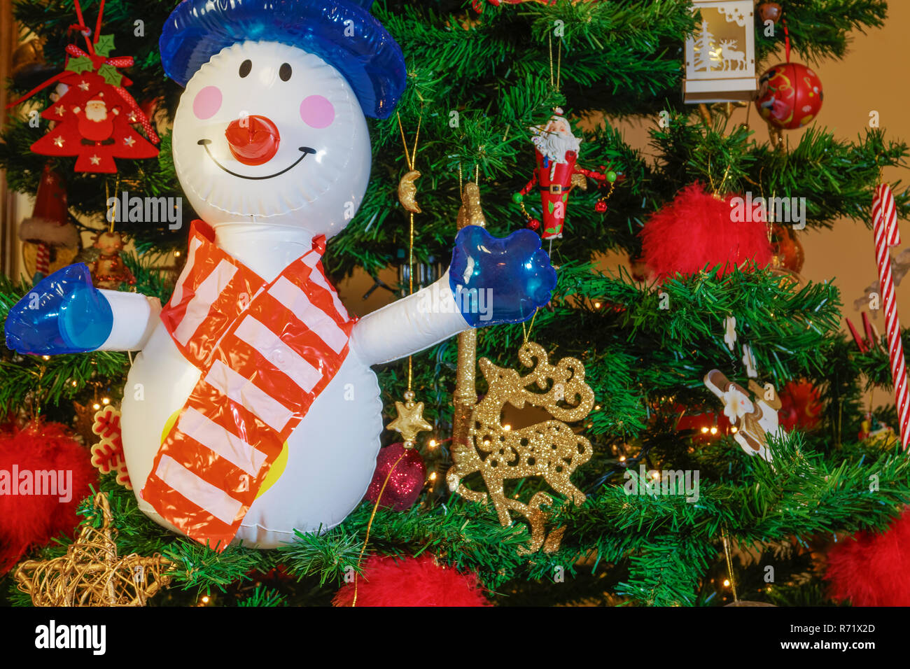 Große aufblasbare Schneemann auf einen Weihnachtsbaum. Luft ausgeblasen saisonale Abbildung, bevor eine beleuchtete künstlicher Weihnachtsbaum mit Lichtern und Dekorationen. Stockfoto