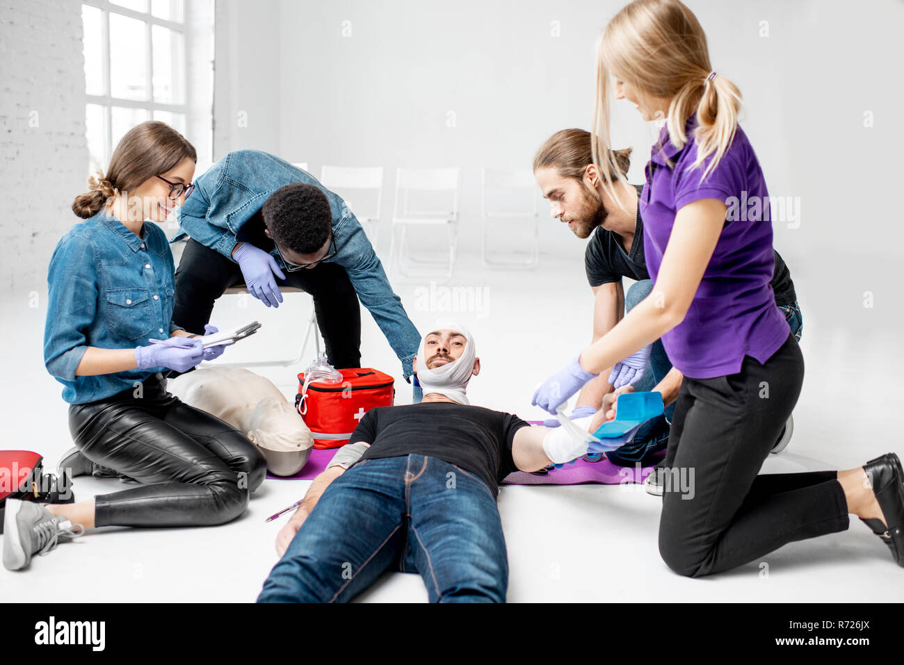 Gruppe von jungen Menschen, die während der Erste Hilfe Schulung mit Kursleiter, die zeigen, wie eine Bandage auf verletzte Person zu gelten Stockfoto