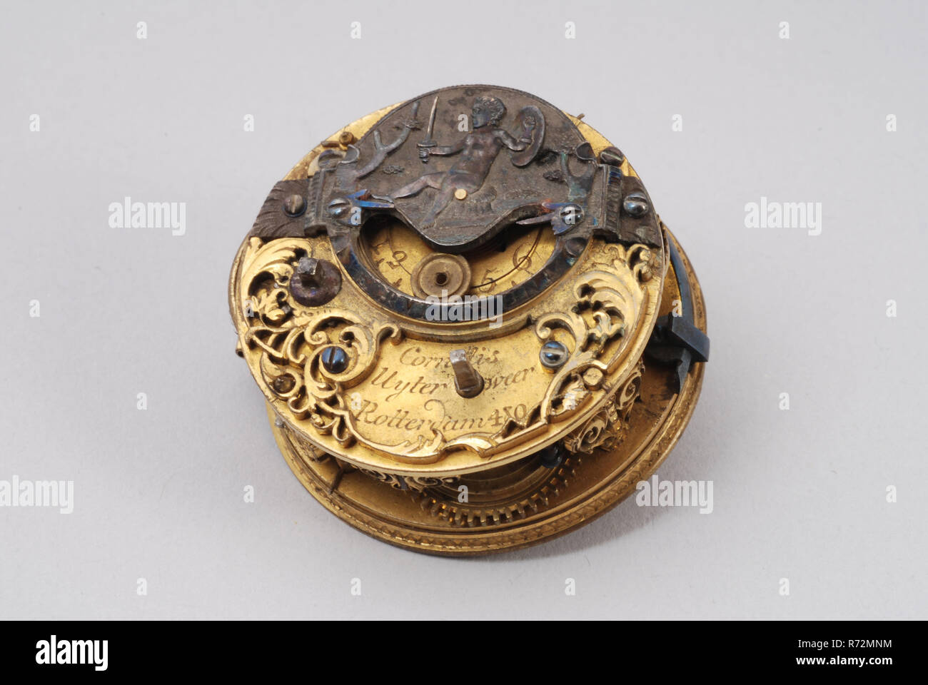 Cornelius Uyterweer, die Innenseite der Taschenuhr mit auf Lücke bild Kind mit Schwert und Schild und SERVIAT UNI geschrieben, Pocket Watch Uhrwerk Messgerät gold Messing Stahl d 2,4, die Bewegung mit Spindel und Schnauze fächerförmigen Säulen an der Oberseite - gesägt Markise für die snek. Auf der Rückseite der Platte Silber geschlossen Brücke mit angetriebenen Darstellung von Kind sitzen auf Hocker mit Schwert und Schild. Unter der Niere-förmige Öffnung für die Glasscheibe der Text: SERVIAT UNI. Hinter den sichtbaren Teil der Balance in Form von Genuteten objektiv. Neben der Schlucht square gebläute Tipp für die regulage. Gut-wo Stockfoto