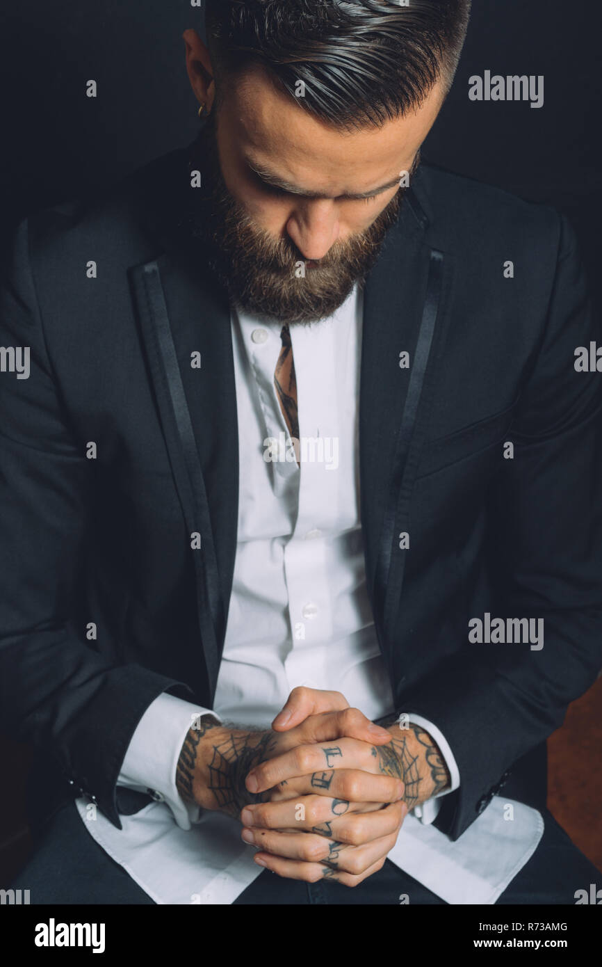Junger Mann mit Anzug, mit gefalteten Händen, Tattoos auf Hände,  nachdenklichen Ausdruck Stockfotografie - Alamy