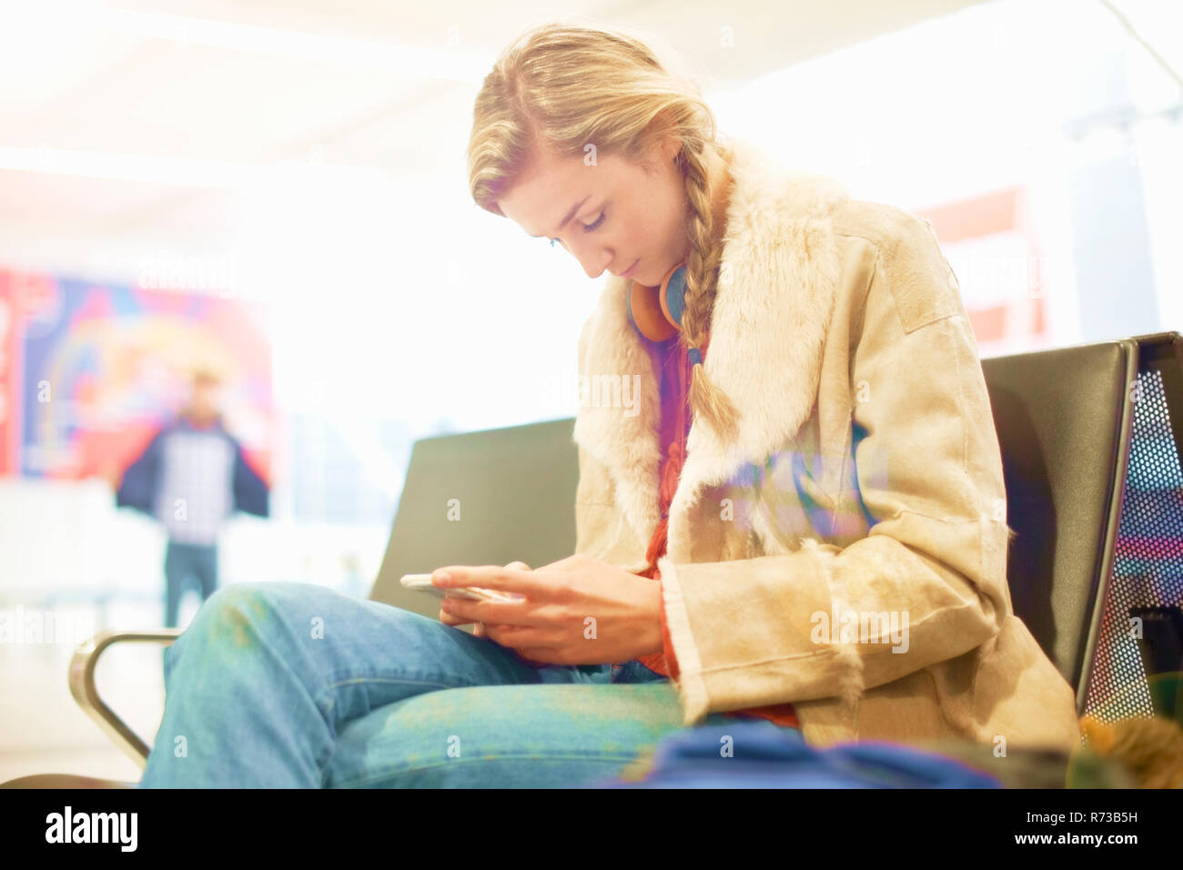 Junge Frau am Flughafen, sitzend, mit Smartphone Stockfoto