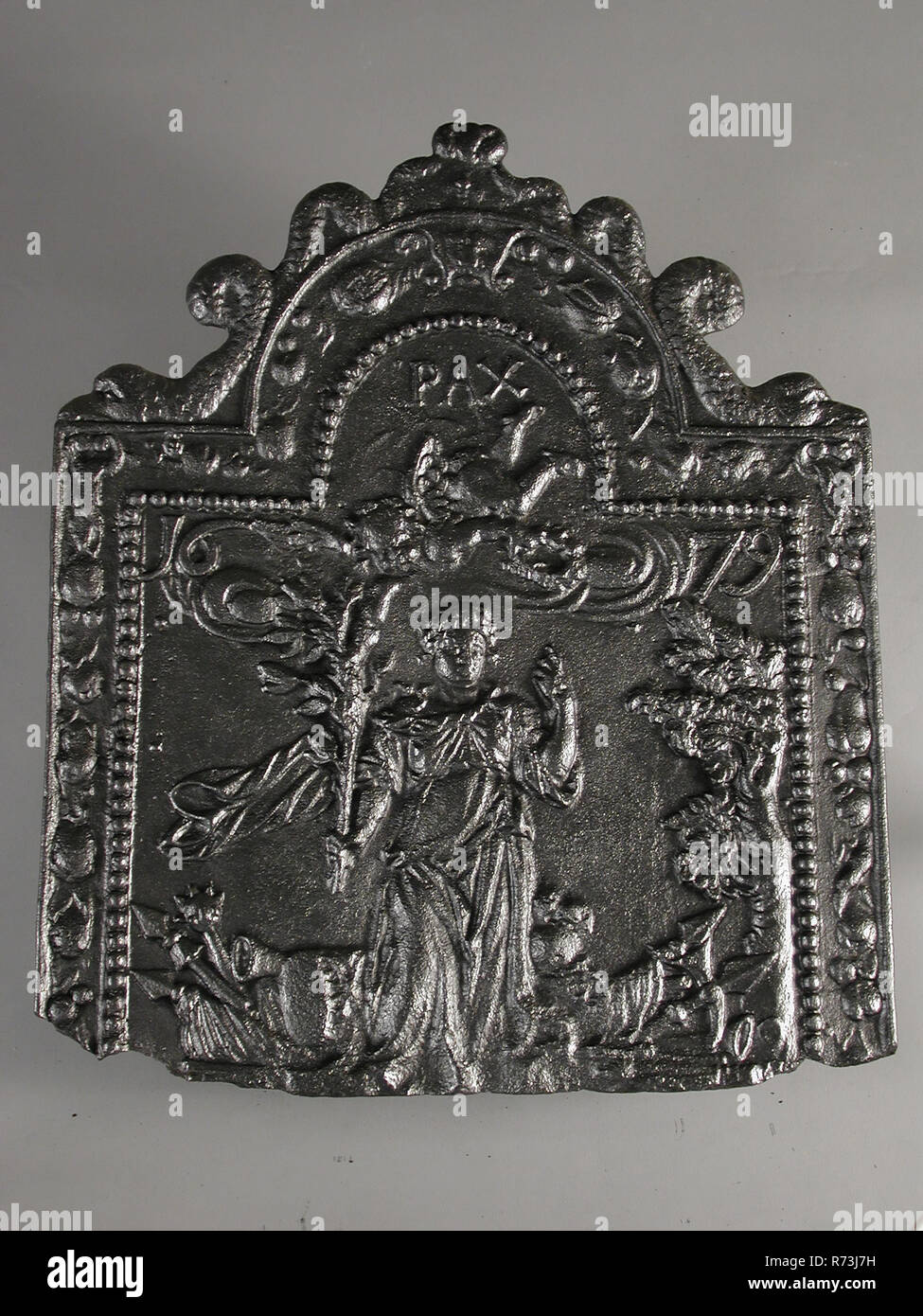 Fireback weibliche Figur Frieden, Jahr 1679, PAX, Kamin Eisen, Gusseisen rechteckig mit Bogen an der Spitze. Auf der Oberseite von zwei Delphinen Kante zwischen Rahmen und Perlenkette mit Obst Kleiderbügel. Auf dem mittleren Bild der Frau in der Landschaft der linke Arm mit erhobenen Zeigefinger nach oben; in der rechten Hand Blume Zweig über der Frau ein Engel mit Girlande mit Blumen fliegen unter ihren Füßen alle Arten von Waffen über der Engel Text; auf beiden Seiten der Frau, die das Jahr angibt, oberhalb der Engel: PAX; auf beiden Seiten der Frau: 1679 Lebensraum Innenraumheizung Rotterdam Dreieck Peperstraat Frieden Aus Stockfoto