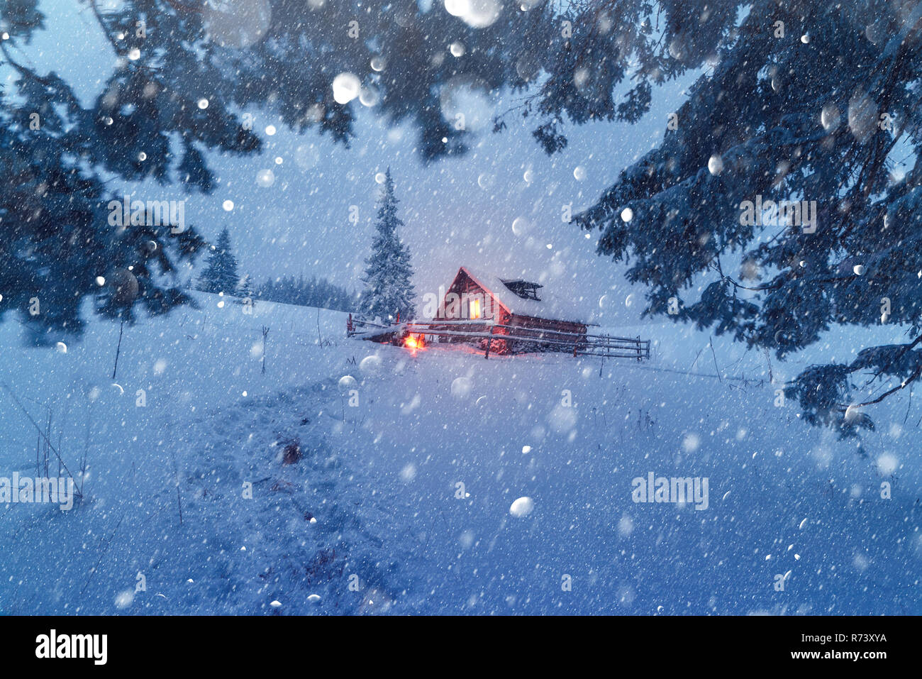 Fantastische Szene mit schneebedeckten Haus am Wald. Licht im kleinen Fenster. Weihnachten Postkarte Collage. DOF bokeh Licht postprocessing Effekt Stockfoto