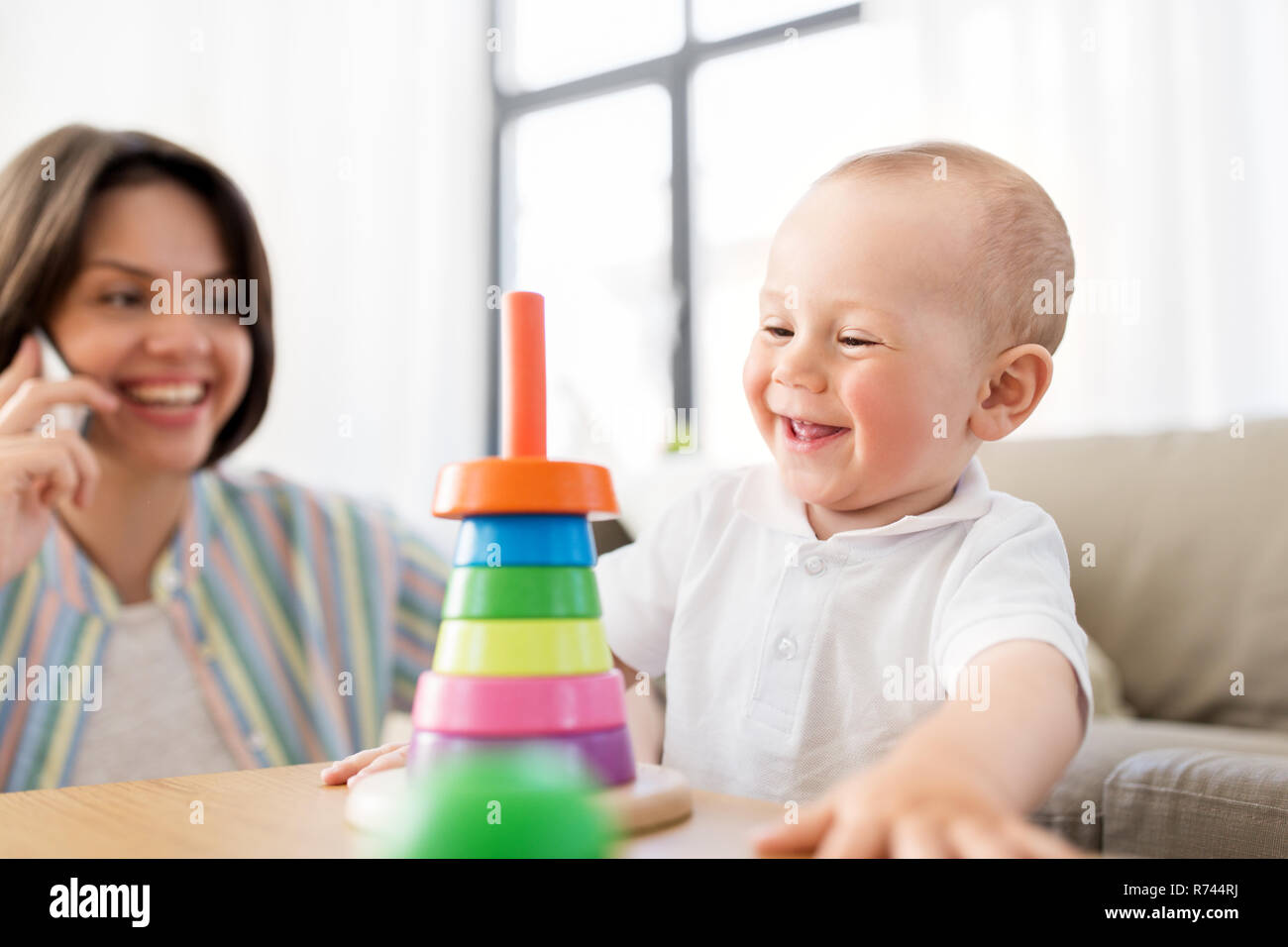 Baby spielen Spielzeug und Mutter ruft auf dem Smartphone Stockfoto