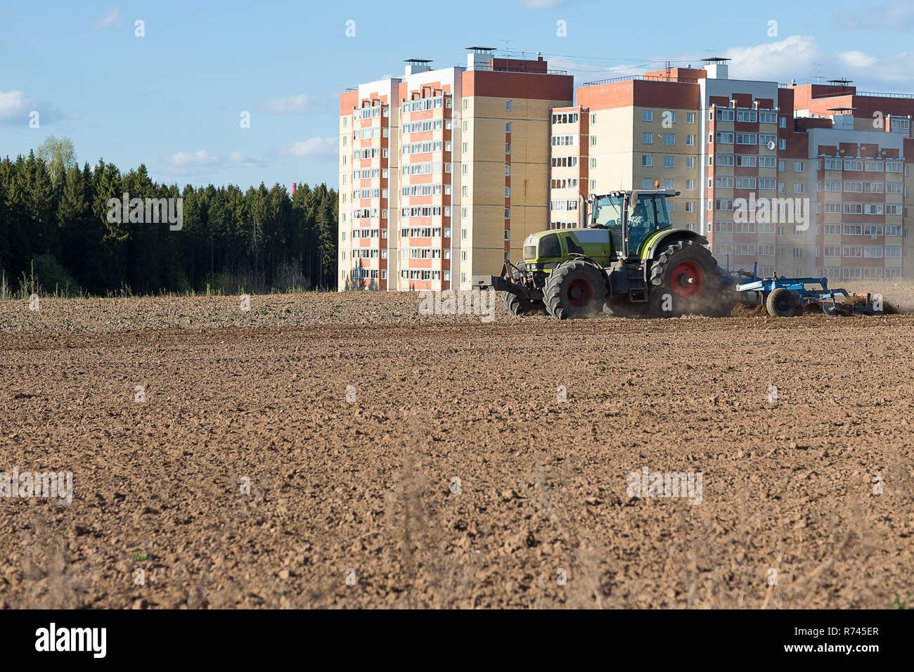 Die Industrialisierung der Weiten. Traktor pflügen landen auf dem Hintergrund der Häuser im Bau. Stockfoto