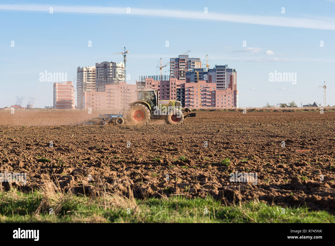 Die Industrialisierung der Weiten. Traktor pflügen landen auf dem Hintergrund der Häuser im Bau. Stockfoto