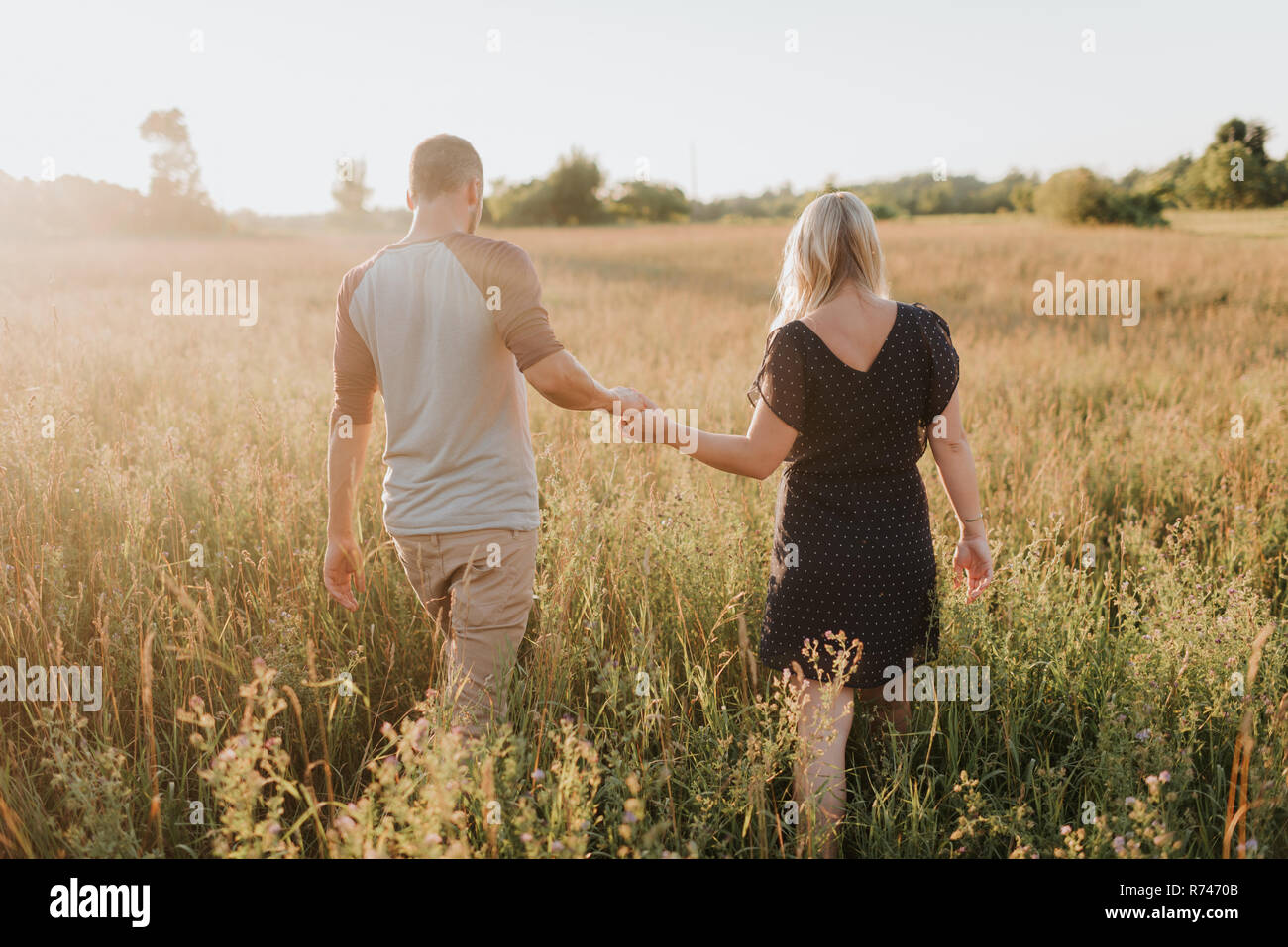 Romantischer Mann und Freundin im Bereich der Sonnenbeschienenen langes Gras bummeln, Rückansicht Stockfoto