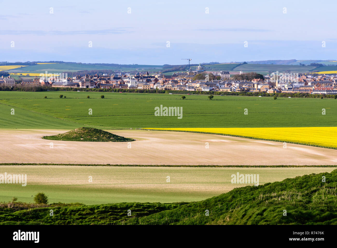 Eine alte runde Barrow steht in einem Bauernhof Feld in Dorset, neue Häuser zu bauen und den Bau des neuen Dorchester Vorort von poundbury in der Rückseite Stockfoto