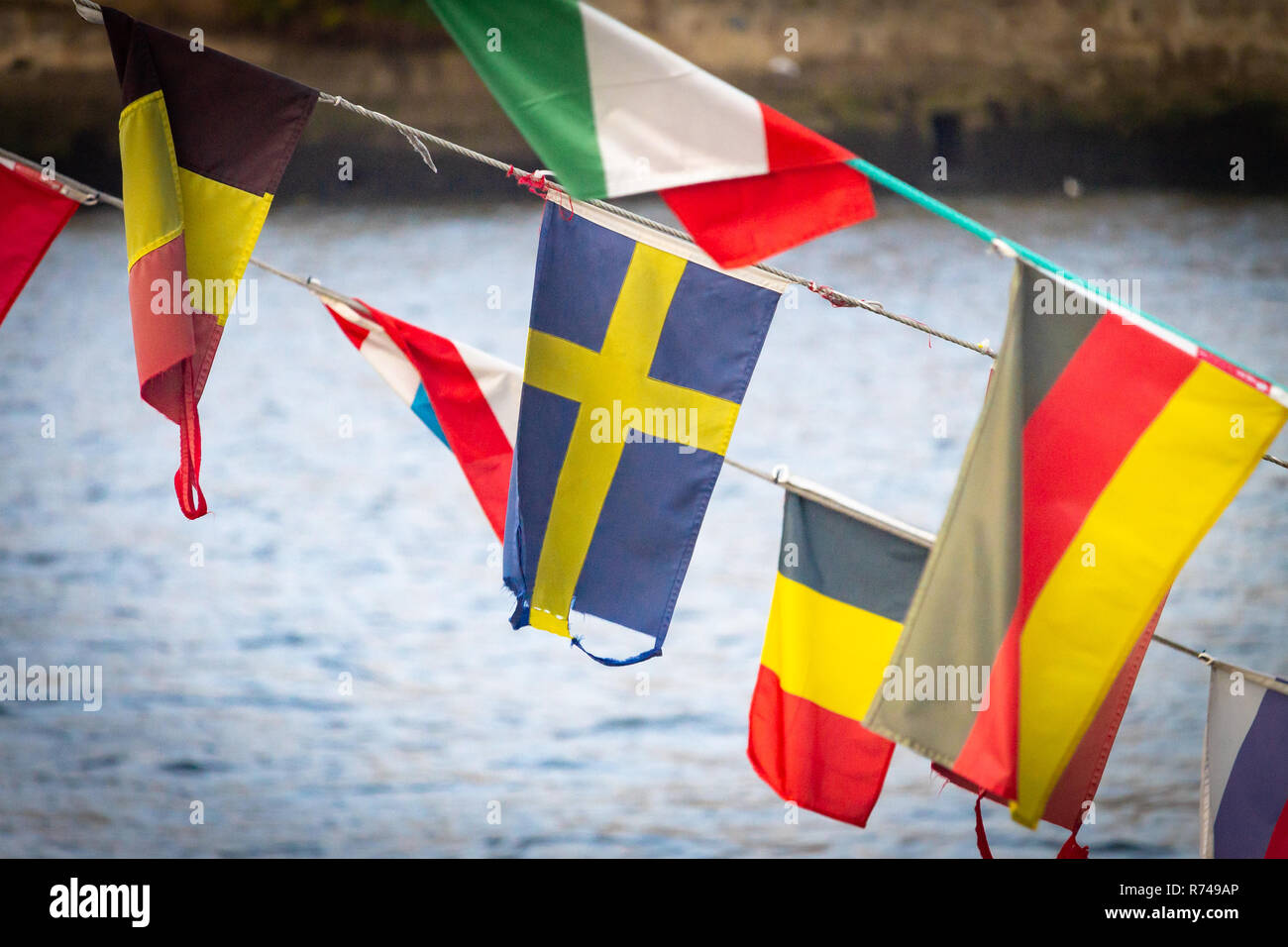 Eine Flagge Schwedens Wellen inmitten von anderen nationalen Flaggen (Belgien, Deutschland, Italien), gegen ein Fluss im Hintergrund. Stockfoto