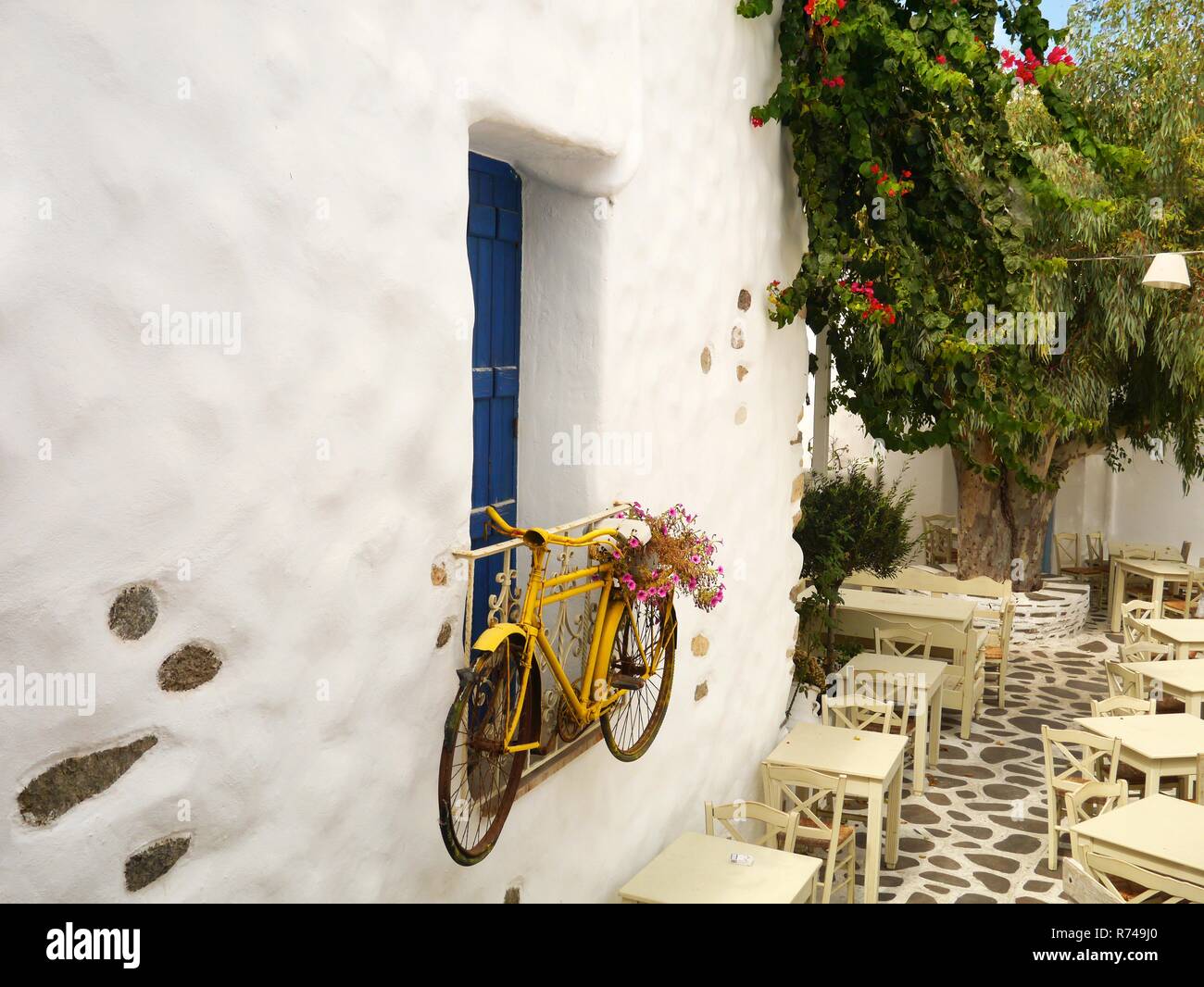 Dekorative Fahrrad hängen an einem Fenster an einem externen Restaurant mit Tischen und einem schönen blühenden Baum Stockfoto