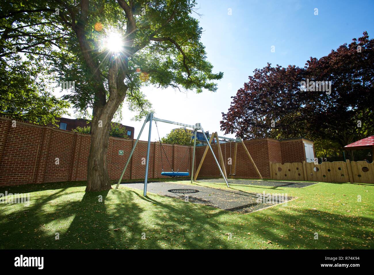 Moderne sicheren Spielplatz mit einem grossen Schwingen Gummimatte und Kunstrasen in einem geschlossenen Hof an einem sonnigen Tag. Stockfoto