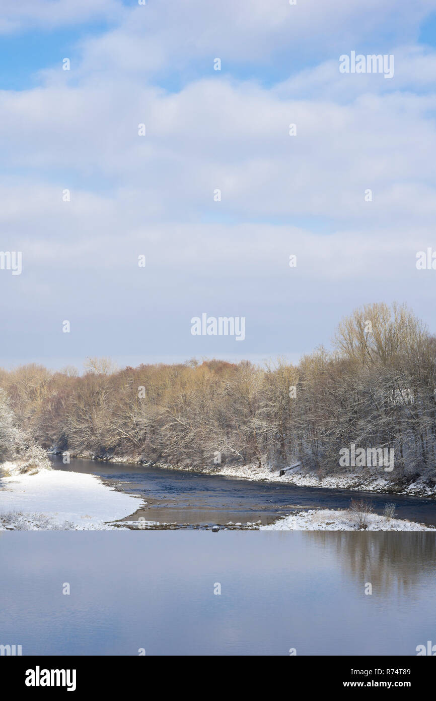 Blick auf einem Fluss und Bäume vor einem blauen Himmel mit weißen flauschigen Wolken im Winter. Stockfoto