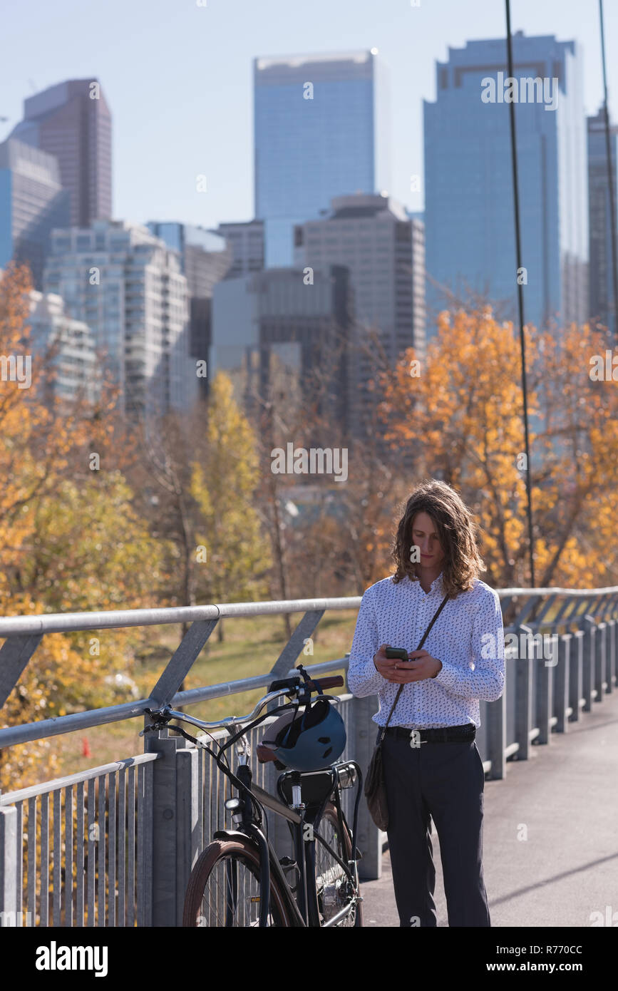 Mann mit Handy beim Stehen mit dem Fahrrad auf der Brücke Stockfoto