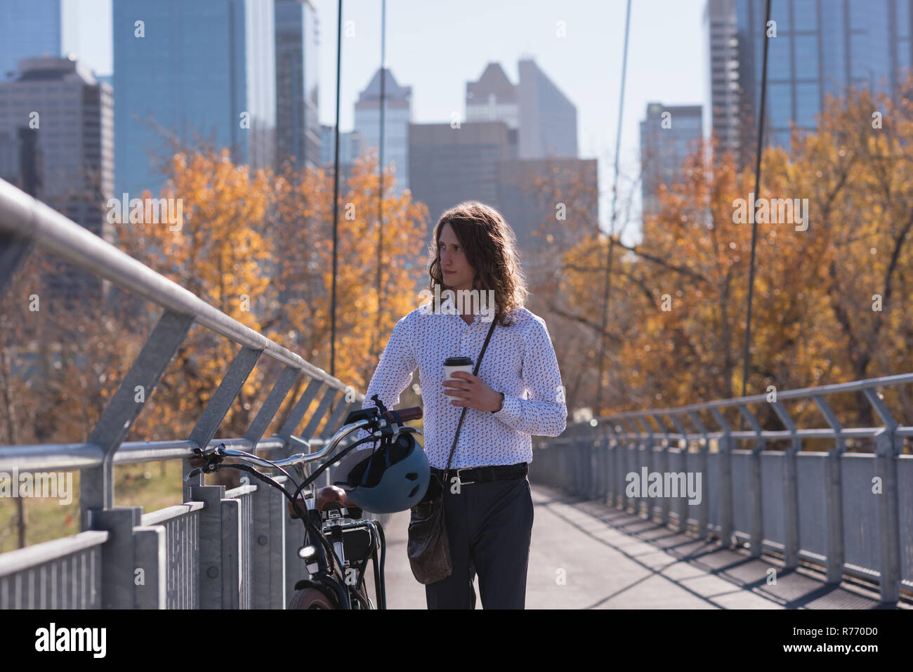 Mann mit Handy beim Gehen mit dem Fahrrad auf der Brücke Stockfoto