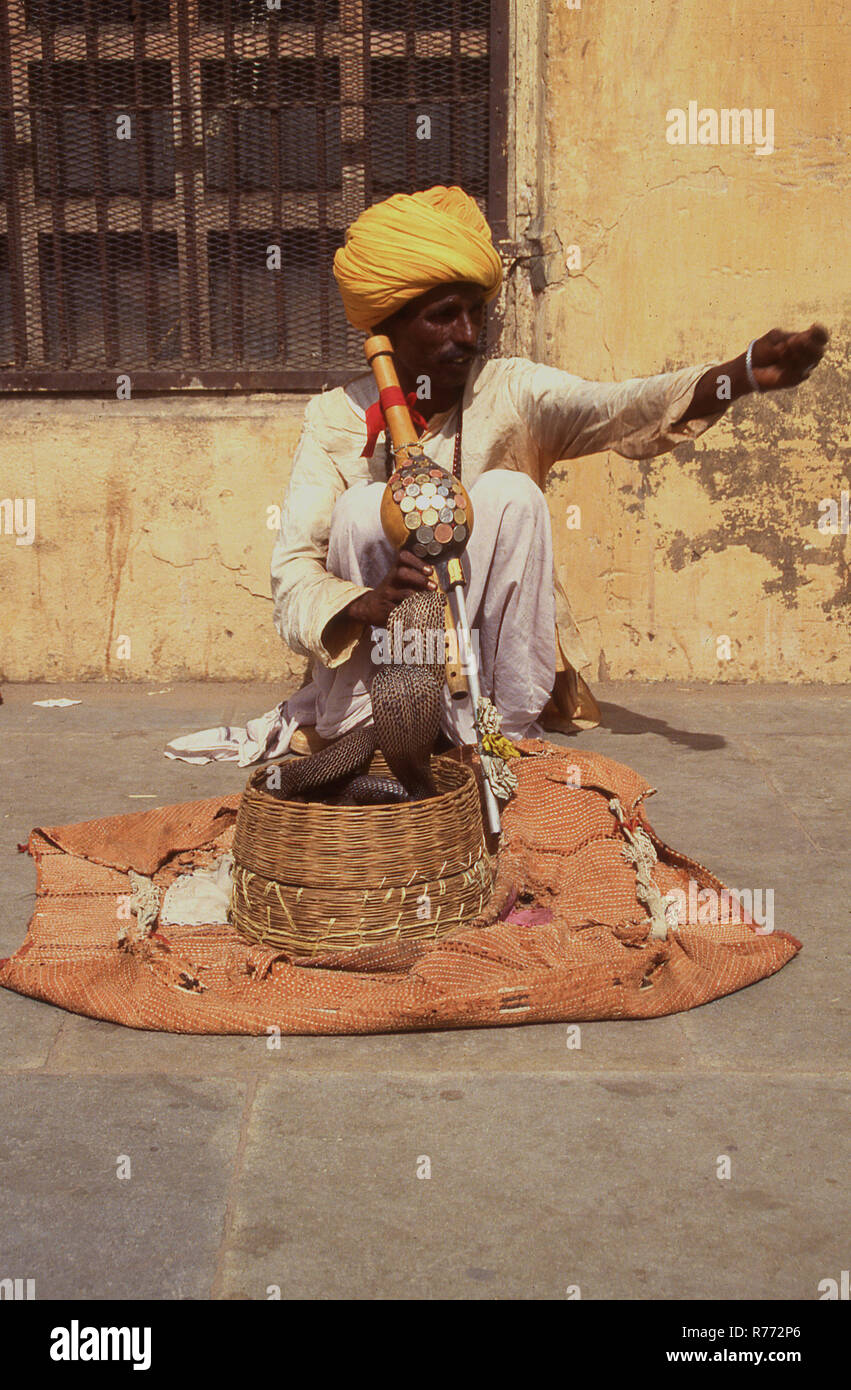 1960, historische, eine indische Schlangenbeschwörer in Turban draußen sitzen mit Musikinstrument, ein Kürbis Flöte und mit seiner Schlange in einem Weidenkorb auf eine Wolldecke gelegt. Schlange charmant ist eine uralte indische Volkskunst und vererbt unter Familien wie die Schlangen von Hindus verehrt werden. Stockfoto