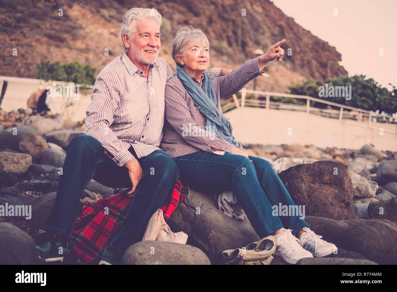 Ältere Leute zusammen in Liebe - ältere Paar aufdem Strand umarmen und Suchen und zeigt mit ausgestrecktem Arm auf den Horizont an Sonnen Stockfoto