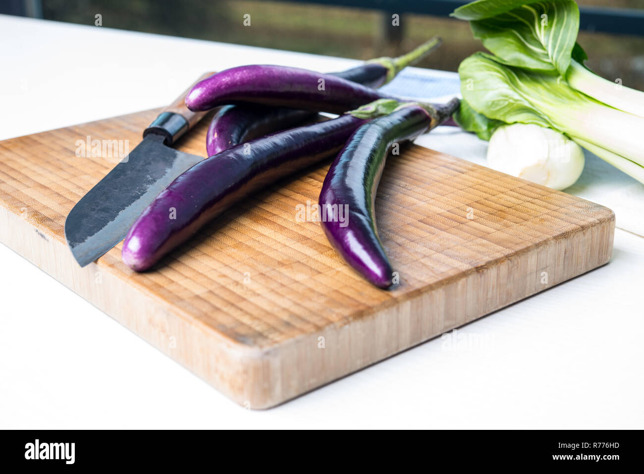 Japanische Aubergine auf Holzbrett mit Messer und Pak Choi Salat Stockfoto