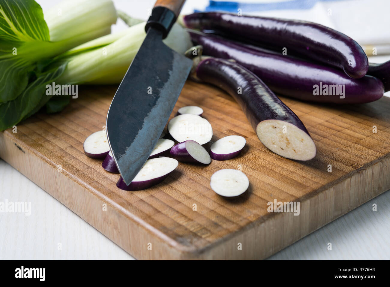 Japanische Aubergine auf Holzbrett mit Messer und Pak Choi Salat Stockfoto