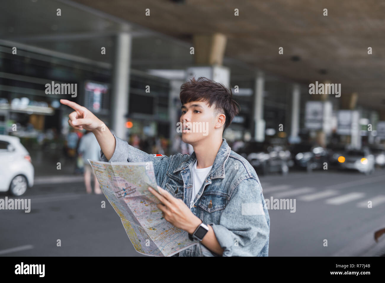 Gut aussehender junger Mann mit Gepäck Tasche auf Stadt Straße mit viel Verkehr Verkehr Suche Karte, Warten auf dem Bus Stockfoto