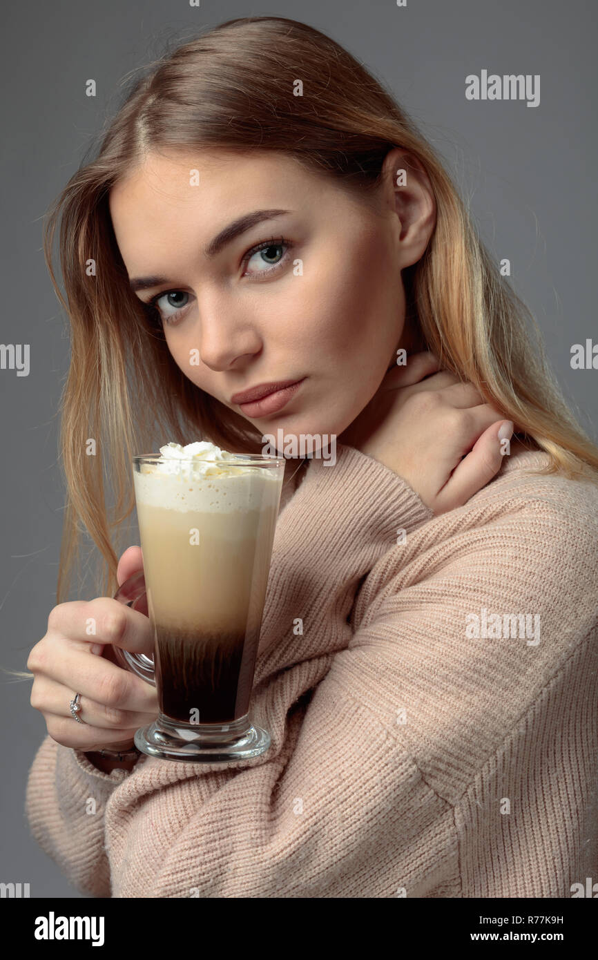 Attraktive junge frau mit Irish Coffee. Schöne Blondine in einem Pullover mit einem Becher Kaffee mit Sahne. Stockfoto