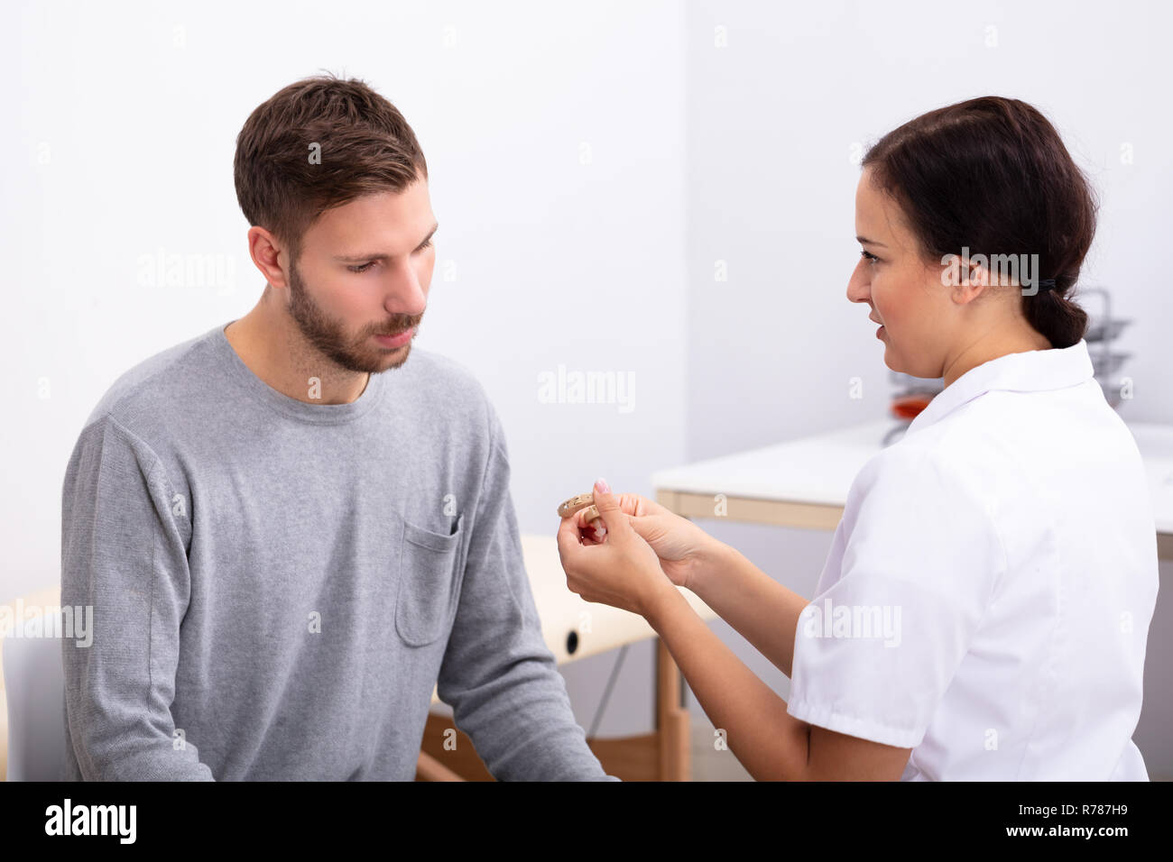 Junge männliche Patienten Betrachten Ärztin Holding Hörgerät In der Klinik Stockfoto