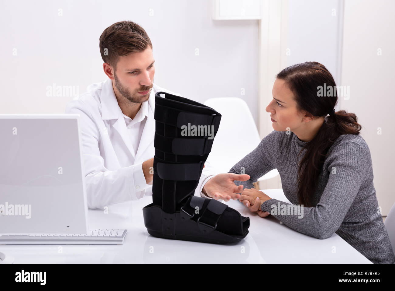 Arzt und Patientin Sitzen in Klinik mit Fuß Bandage auf Schreibtisch Stockfoto