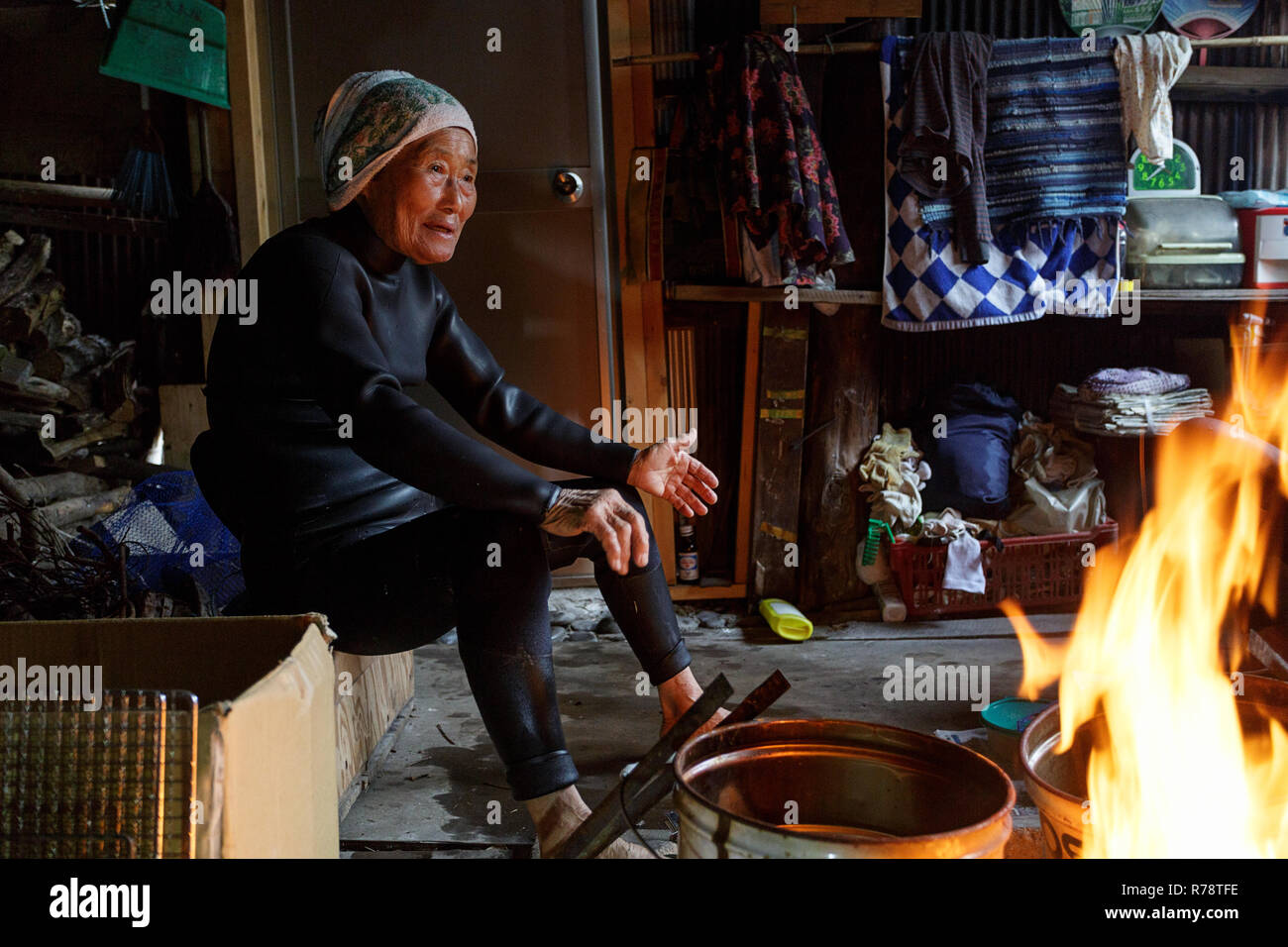 Ama Taucher im Neoprenanzug entspannen, plaudern und Aufwärmen am Kamin in ihren traditionellen Holzhütte nach einem Tauchgang im Meer, Mie, Japan Stockfoto