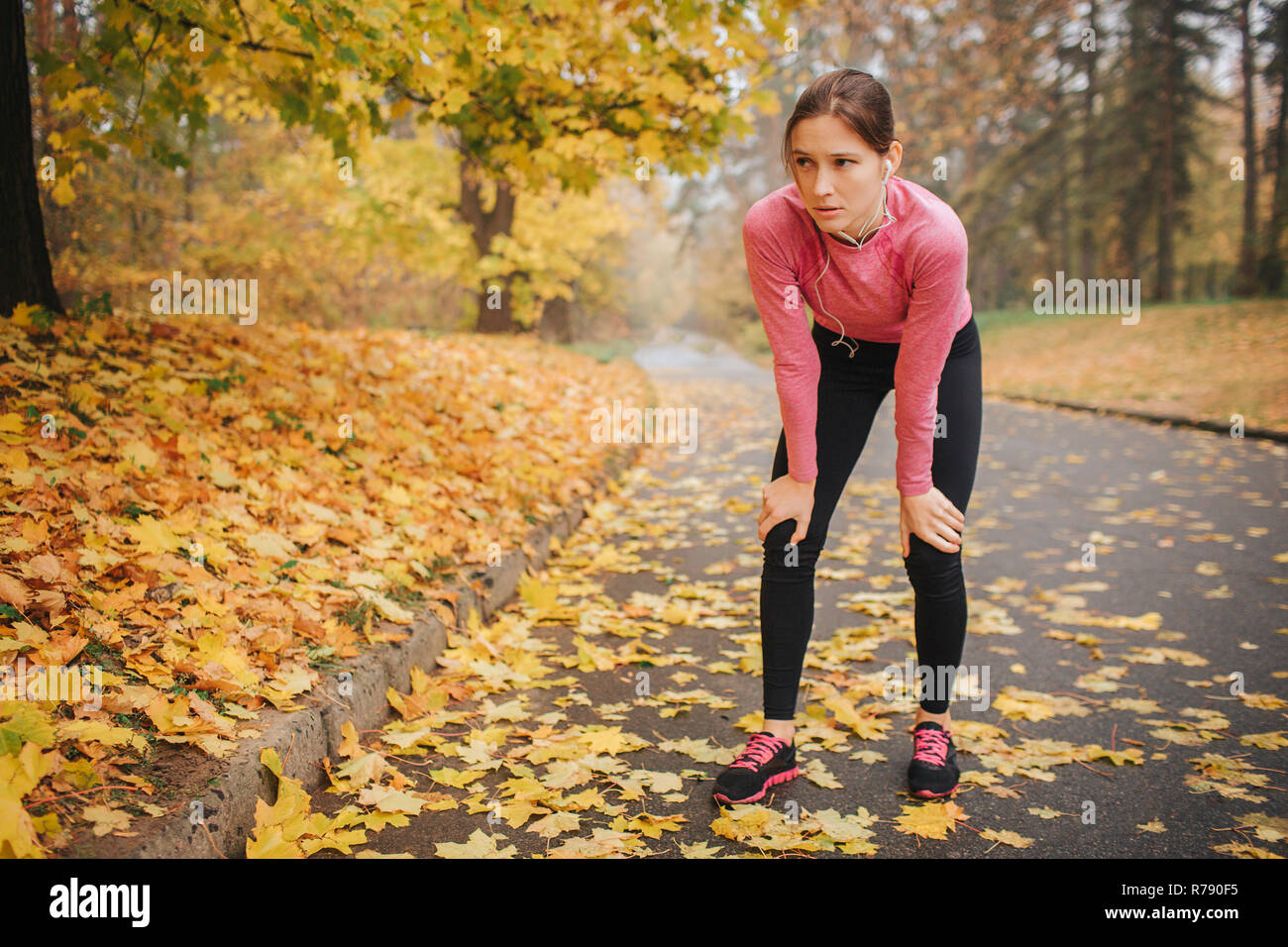 Müde und erschöpft junge Frau steht und hat Ruhe. Sie hält die Hände auf den Knien. Modell auf der Straße allein. Sie hören Sie Musik über Kopfhörer. Stockfoto