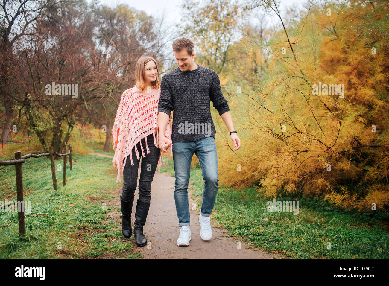 Junger Mann und Frau gehen gemeinsam in den Park. Sie halten einander die Hände. Stockfoto